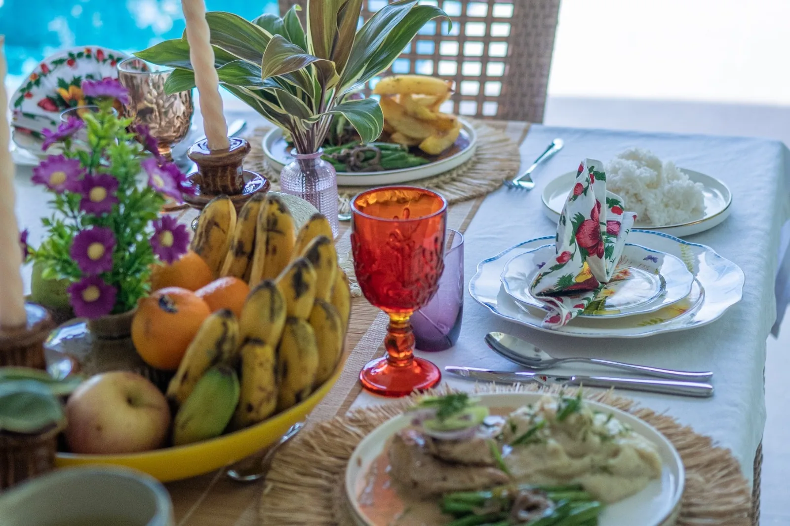 A colourful table set for a meal at Villa Kulintang, with tropical fruit and the pool beyond