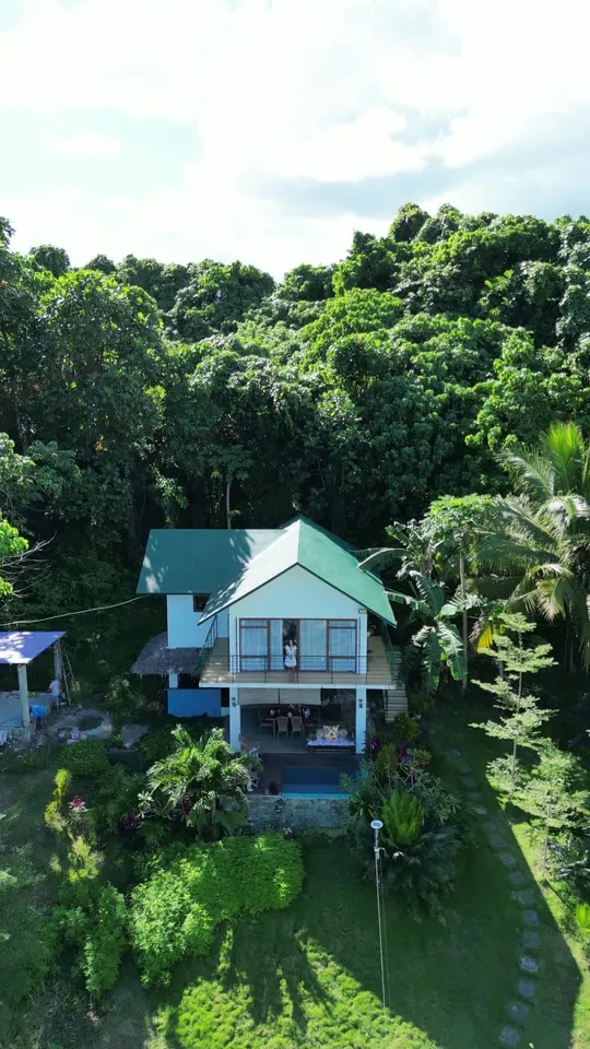 The villa framed by tropical forest, seen from a slowly retreating drone